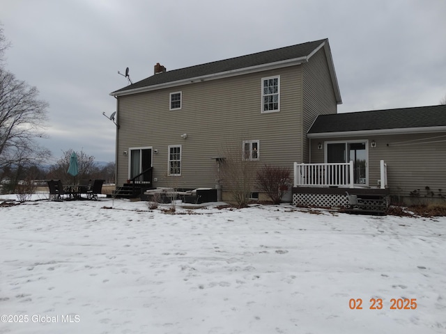 snow covered back of property with entry steps and a chimney