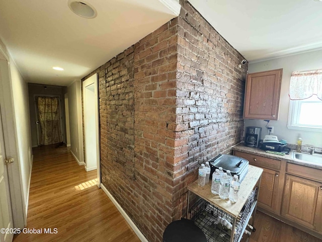 kitchen with brown cabinets, dark wood finished floors, a sink, and brick wall