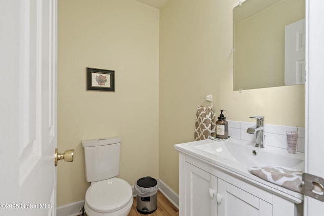 half bathroom with toilet, wood finished floors, vanity, and baseboards