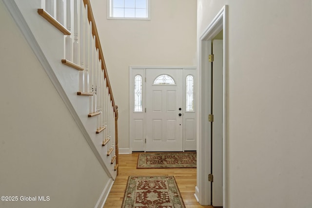 entrance foyer with light wood finished floors, stairs, a high ceiling, and a wealth of natural light