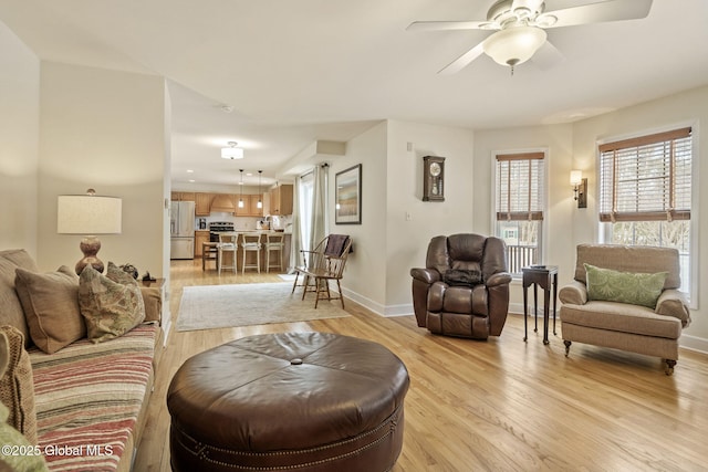 living area featuring light wood-style floors, baseboards, and a ceiling fan