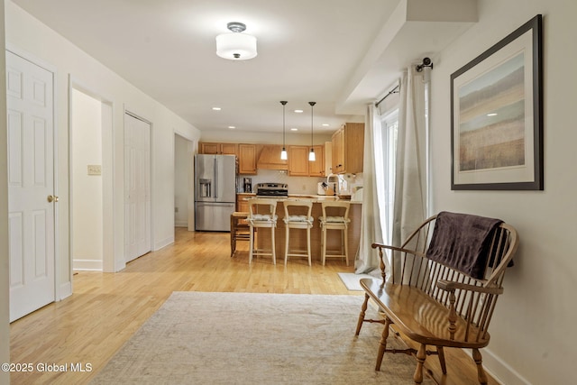 interior space featuring baseboards, light wood-style flooring, appliances with stainless steel finishes, hanging light fixtures, and custom exhaust hood