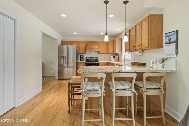 kitchen with a peninsula, a sink, appliances with stainless steel finishes, light wood-type flooring, and backsplash