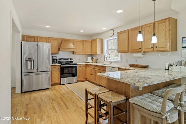 kitchen featuring a peninsula, stainless steel appliances, light wood-type flooring, premium range hood, and a sink