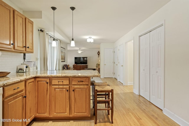 kitchen featuring a peninsula, light stone countertops, hanging light fixtures, light wood-type flooring, and backsplash