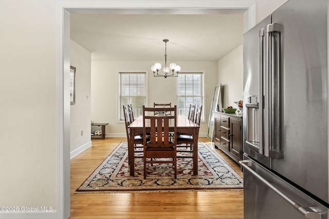 dining area with baseboards, light wood finished floors, and an inviting chandelier