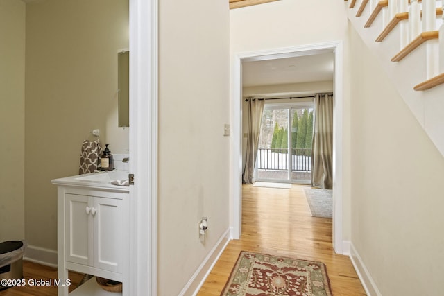 hall with baseboards, stairway, and light wood finished floors