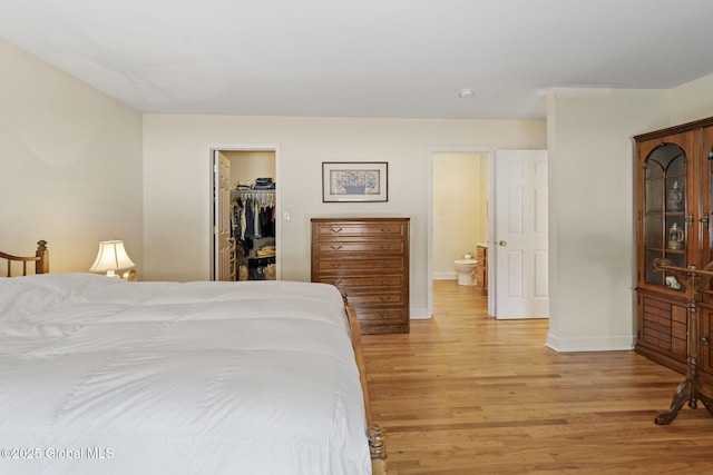 bedroom featuring a spacious closet, a closet, light wood-style flooring, and baseboards