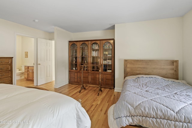 bedroom with ensuite bath, light wood-style flooring, and baseboards