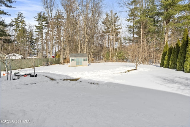 yard layered in snow with a storage shed, fence, and an outdoor structure