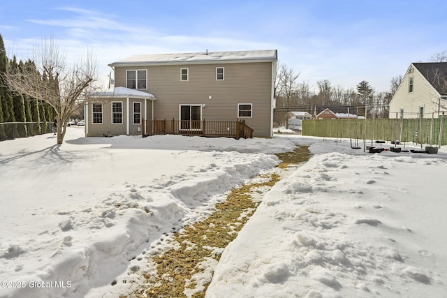 snow covered house featuring fence and a wooden deck