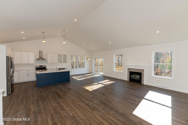 kitchen featuring a center island with sink, light countertops, open floor plan, white cabinetry, and wall chimney range hood