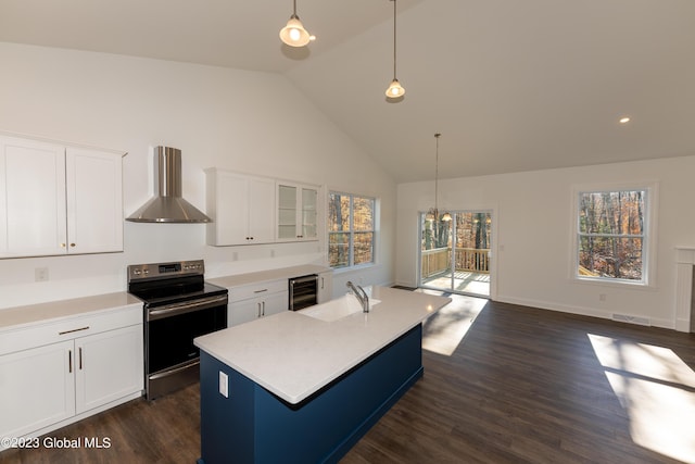 kitchen with a center island with sink, light countertops, glass insert cabinets, wall chimney range hood, and stainless steel range with electric stovetop