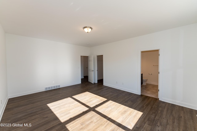 unfurnished bedroom featuring dark wood-type flooring, visible vents, baseboards, and ensuite bathroom