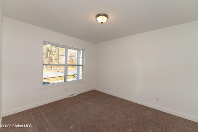 unfurnished room featuring visible vents, dark carpet, and baseboards