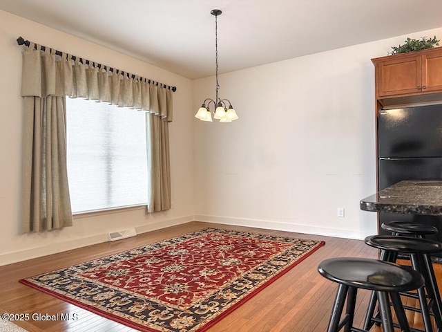 dining space featuring wood-type flooring, visible vents, baseboards, and an inviting chandelier