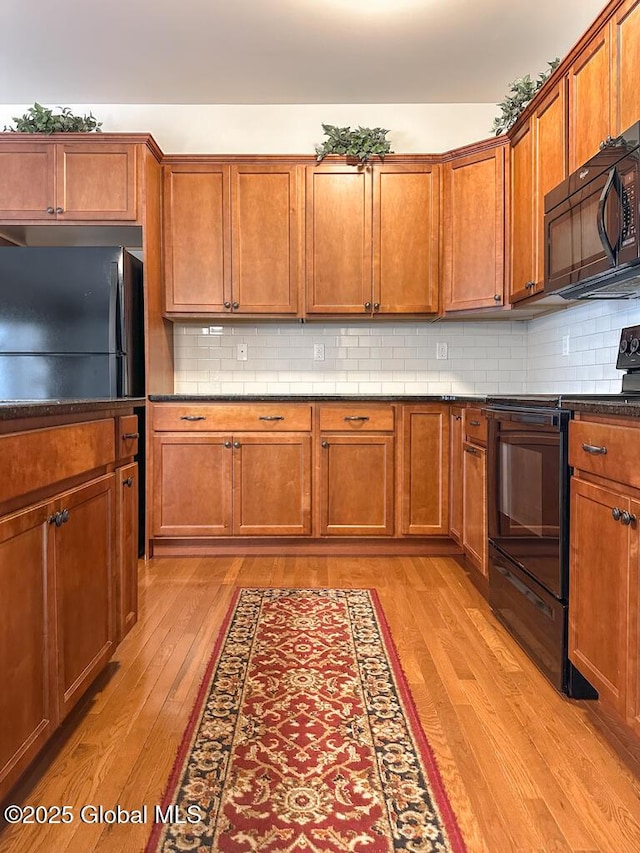 kitchen featuring light wood-style flooring, brown cabinets, black appliances, tasteful backsplash, and dark countertops