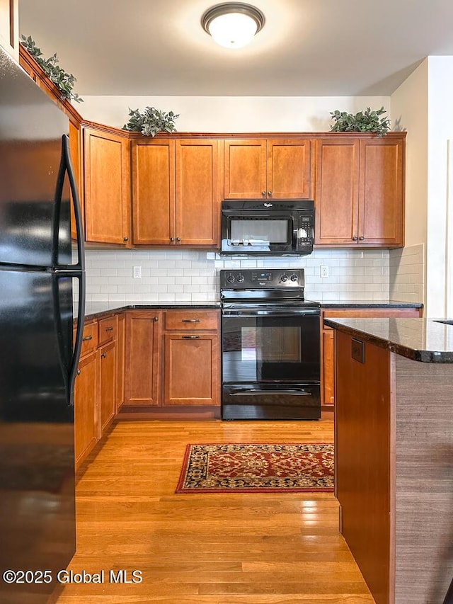 kitchen with decorative backsplash, brown cabinetry, dark stone countertops, light wood-type flooring, and black appliances