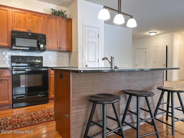 kitchen with black appliances, a kitchen bar, backsplash, and a center island with sink