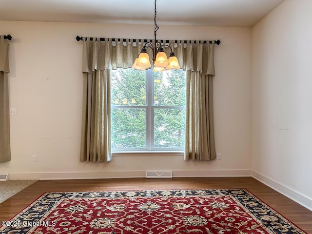 unfurnished dining area with dark wood-style floors, a healthy amount of sunlight, visible vents, and a notable chandelier