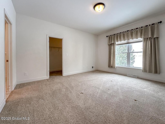 unfurnished bedroom featuring light carpet, baseboards, visible vents, a spacious closet, and a closet