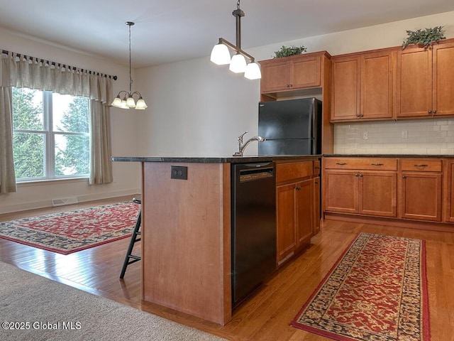 kitchen with a kitchen island, black appliances, brown cabinetry, dark countertops, and a kitchen bar