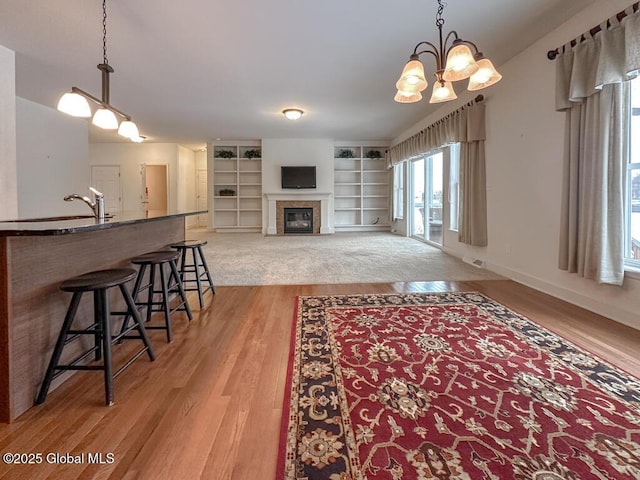 living area with built in shelves, a tile fireplace, baseboards, light wood-type flooring, and an inviting chandelier