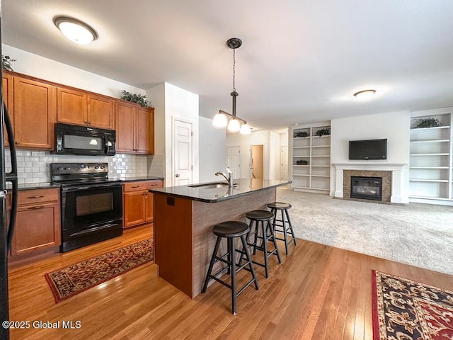 kitchen featuring a center island with sink, brown cabinets, open floor plan, black appliances, and a kitchen bar