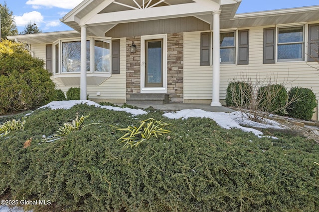 snow covered property entrance featuring stone siding