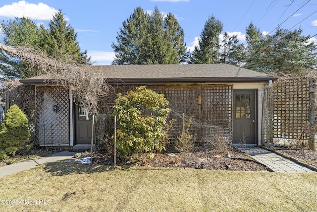 property entrance with a shingled roof and a lawn