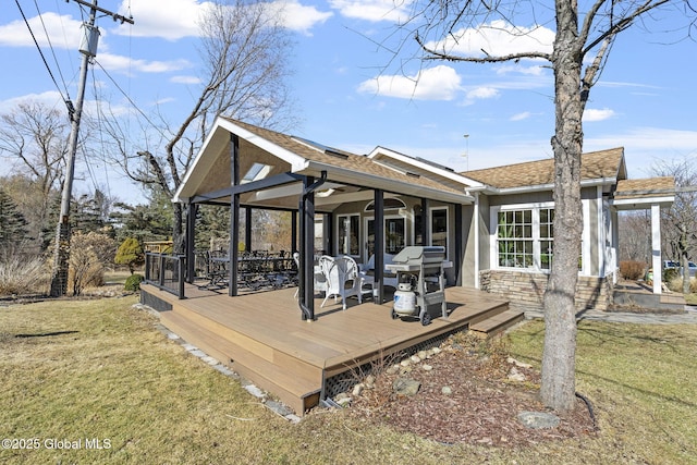 rear view of house with stone siding, a shingled roof, a lawn, and a wooden deck