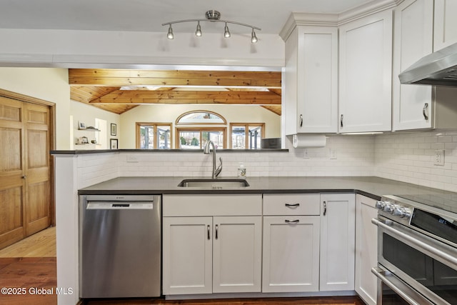 kitchen with vaulted ceiling with beams, stainless steel appliances, a sink, decorative backsplash, and dark countertops