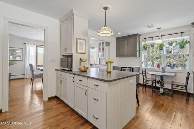 kitchen featuring a baseboard heating unit, dark countertops, wood-type flooring, and visible vents