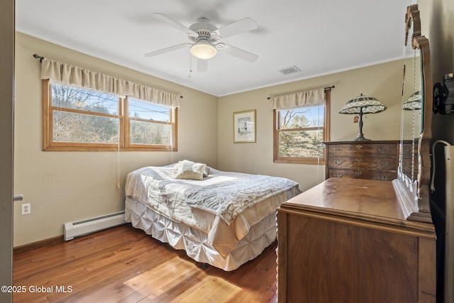 bedroom featuring a baseboard radiator, multiple windows, visible vents, and wood finished floors