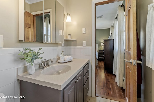 ensuite bathroom featuring ensuite bathroom, vanity, visible vents, and tile walls