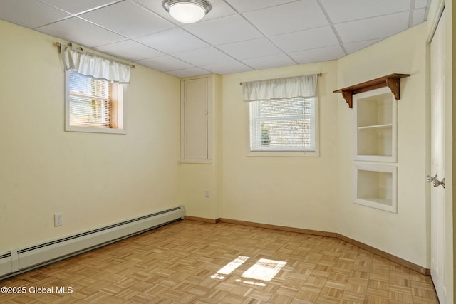 empty room featuring plenty of natural light, a drop ceiling, a baseboard radiator, and baseboards