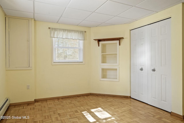 unfurnished bedroom featuring a paneled ceiling, a closet, baseboards, and baseboard heating