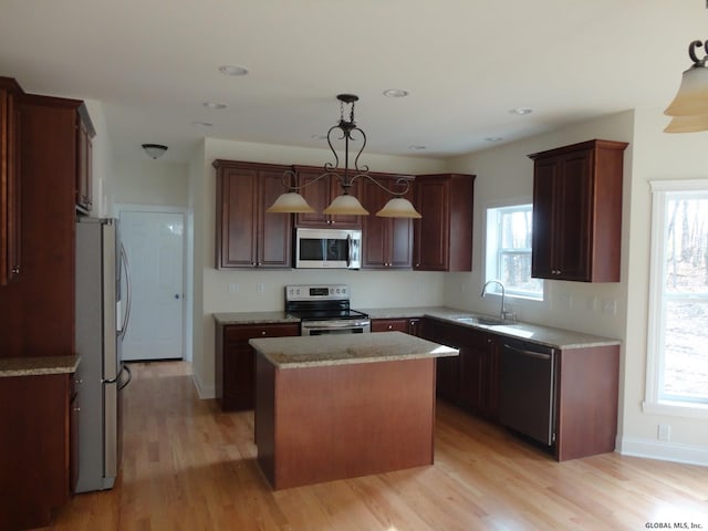 kitchen featuring light wood-type flooring, a sink, a kitchen island, stainless steel appliances, and hanging light fixtures