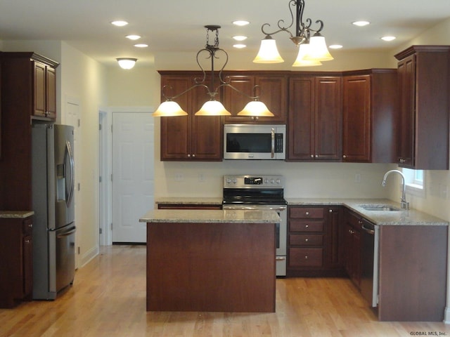 kitchen featuring light stone counters, a kitchen island, light wood-style flooring, a sink, and appliances with stainless steel finishes