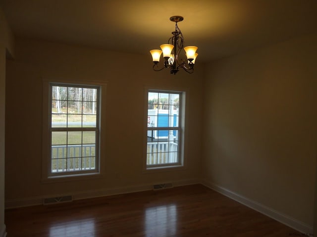 empty room featuring visible vents, baseboards, an inviting chandelier, and dark wood finished floors