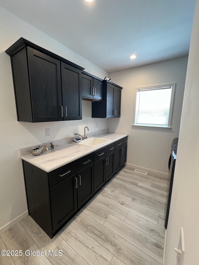 kitchen with light wood finished floors, baseboards, dark cabinets, light countertops, and a sink