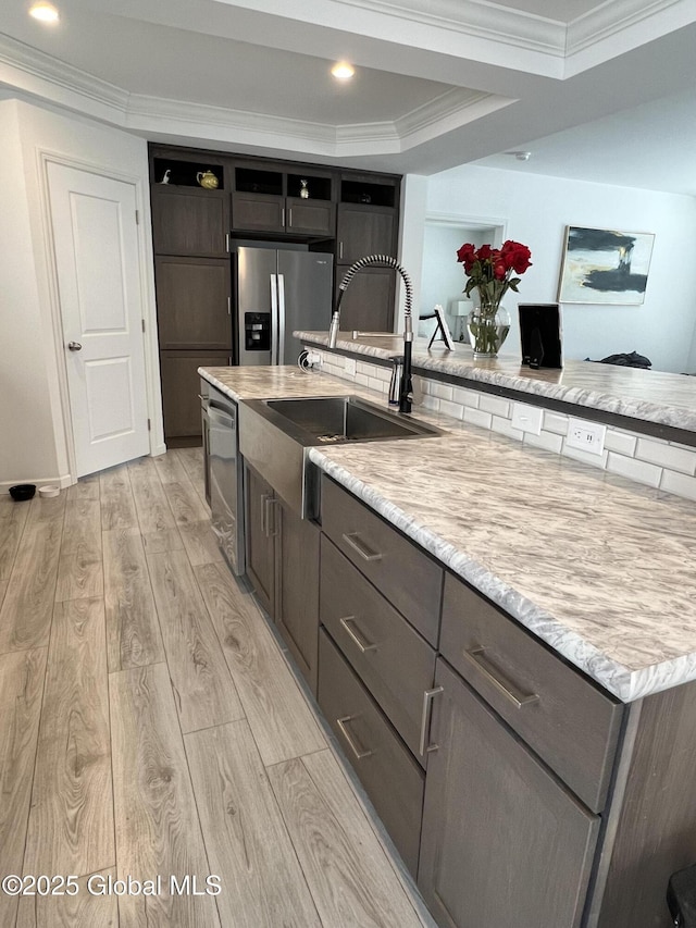 kitchen featuring light stone counters, stainless steel appliances, a sink, light wood-style floors, and crown molding