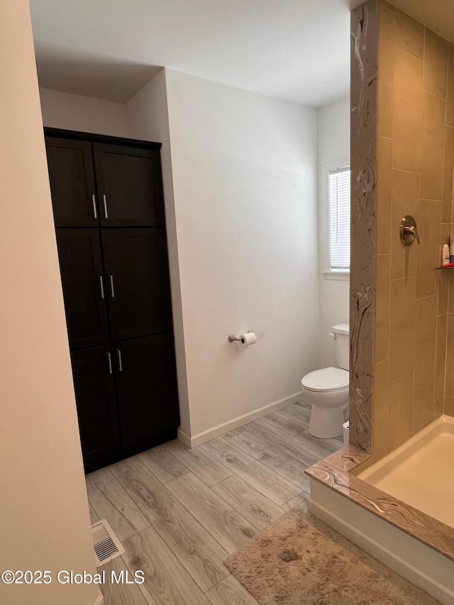 full bath featuring a stall shower, baseboards, toilet, and wood finished floors