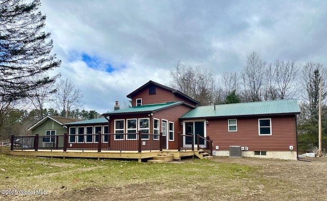 back of property featuring a lawn, central AC unit, a sunroom, metal roof, and a wooden deck