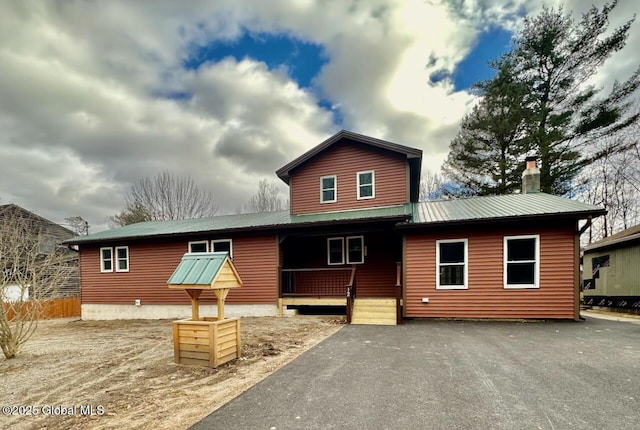 rustic home featuring aphalt driveway, metal roof, a chimney, and a porch