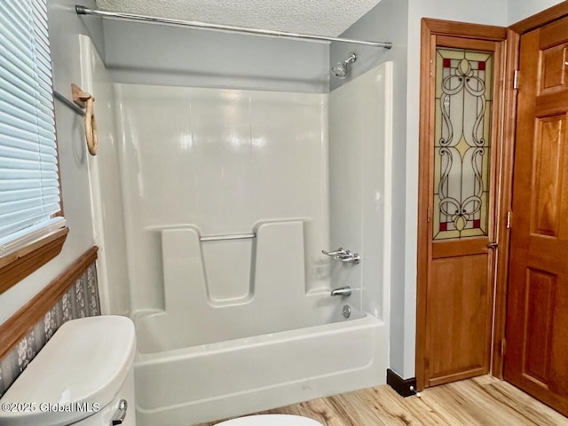 full bathroom with tub / shower combination, a textured ceiling, toilet, and wood finished floors