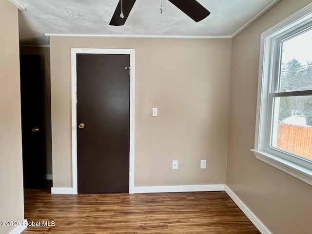 spare room featuring crown molding, wood finished floors, a ceiling fan, and baseboards