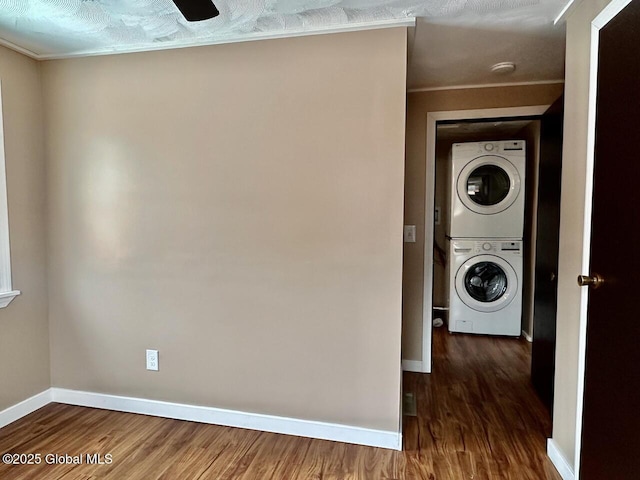 clothes washing area featuring stacked washer / dryer, laundry area, baseboards, and wood finished floors