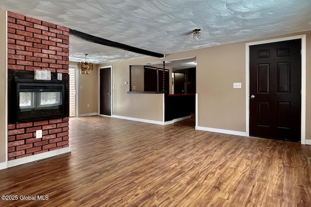 unfurnished living room with an inviting chandelier, a textured ceiling, baseboards, and wood finished floors