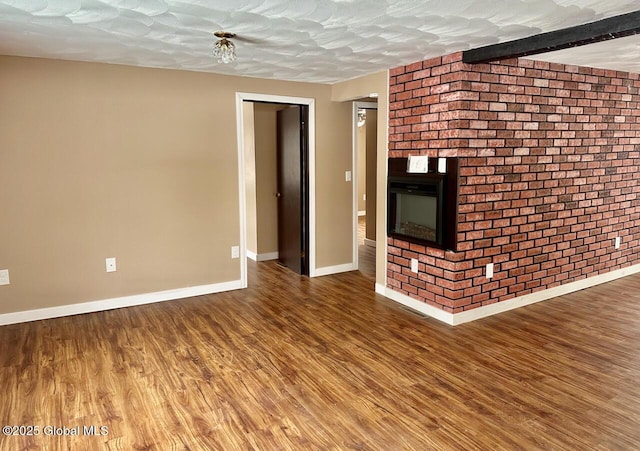 unfurnished living room with a brick fireplace, a textured ceiling, brick wall, wood finished floors, and baseboards